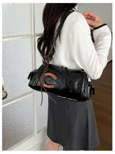 Model wearing a black cylindrical shoulder bag with a woven brown accent and gold-tone hardware