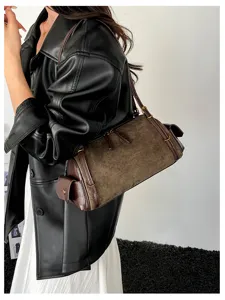 Side view of a woman carrying a brown suede cylindrical bag with dark trim and gold hardware