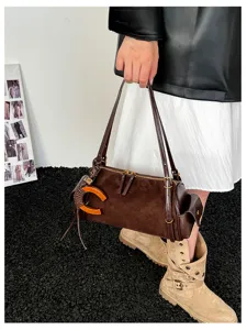 Lifestyle view of a brown suede-look barrel bag held by a model, with an orange C charm and fringe