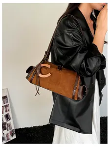 Lifestyle view of a brown suede shoulder bag with dark leather trim, curved metal accent and tassel