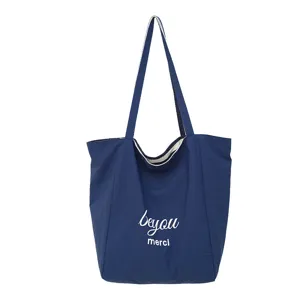 Vista frontal de un bolso de tela azul marino con asas largas y letras blancas «beyou» y «merci»