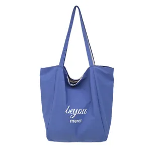 Bolso azul con asas largas y el texto blanco «beyou merci», mostrado sobre un fondo blanco