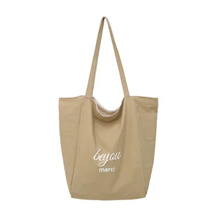 Vista frontal de un bolso beige de tela, con asas largas y las palabras blancas «beyou» y «merci»