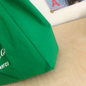 Primer plano de la tela verde arrugada del bolso, con parte del texto blanco « merci » visible
