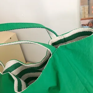 Primer plano de una bolsa tote verde de lona, con asas y forro de rayas blancas y verdes