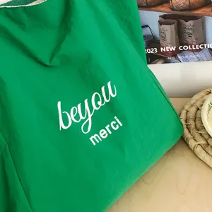 Primer plano de un tote de nailon verde con texto blanco «beyou merci» y tejido ligeramente fruncido