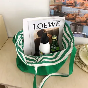 Bolso tote verde abierto con asas de rayas, sobre una mesa de madera junto a revistas y botellas