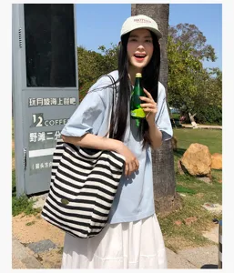 Una mujer lleva al aire libre un bolso amplio de rayas blancas y negras con ropa ligera de verano