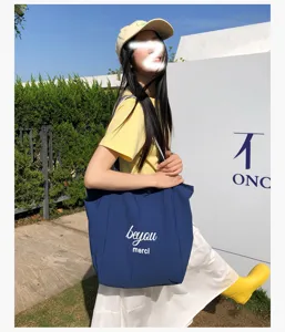 Una mujer lleva al aire libre un bolso azul con letras blancas junto a una pared clara y soleada