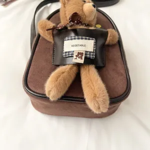 Close-up of brown suede-textured bag, black trim, plush bear charm, and fabric label
