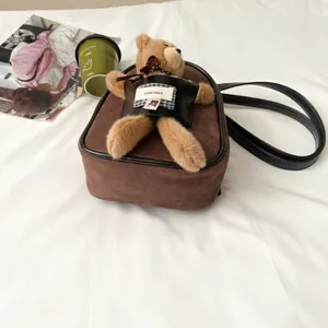 Close-up of a brown suede-textured crossbody bag with a plush bear and black faux-leather trim