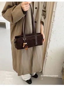 Dark brown suede-look bag with long straps and wooden bead charm, shown carried by a model