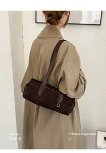 A model wears a brown suede-textured shoulder bag with a long strap and silver D-ring detail