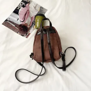 Top-down view of a brown suede-look bag with black straps and gold-tone buckles on white bedding