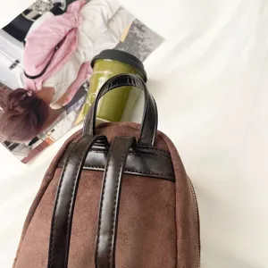 Close-up of a brown suede-textured backpack back with dark faux-leather straps and top handle