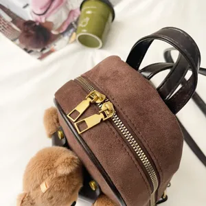 Close-up of a brown suede-look backpack with gold zippers, black straps, and a teddy bear charm
