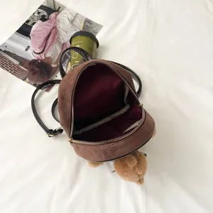 Open brown mini backpack showing its burgundy-lined interior, zip closure and plush bear charm.