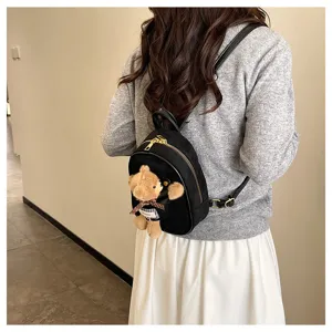 Back view of a woman wearing a black suede-look backpack with gold zipper and teddy bear charm