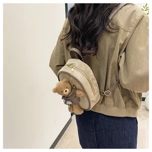 Back view of a model wearing a beige suede mini backpack with a brown teddy bear charm