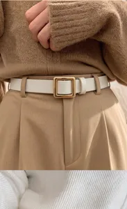 Nahaufnahme eines weißen Gürtels mit goldener eckiger Schnalle über beiger Hose und Strickpullover