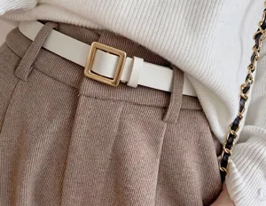 Nahaufnahme: weißer Ledergürtel mit goldener eckiger Schnalle zu karierter Hose und Strickpullover