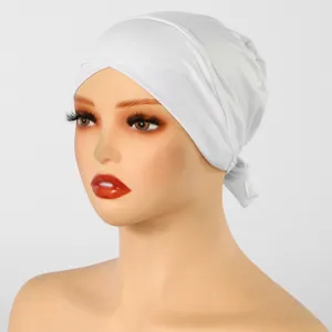 Modèle portant un couvre-chef blanc extensible noué à l’arrière, devant un fond clair uni.