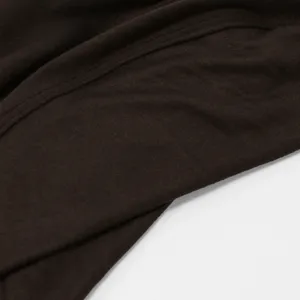 Gros plan sur la texture fine du tissu tricoté brun foncé, avec couture visible et plis souples