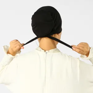 Vue arrière d’une personne qui noue les longs liens noirs d’un bonnet en maille extensible