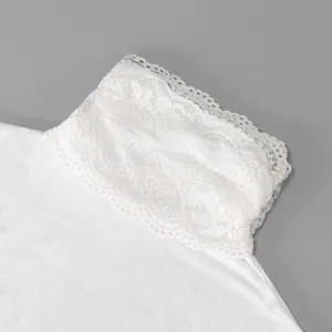 Close-up of a white floral lace collar joined to soft knit fabric against a plain gray background