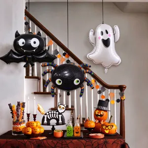 Indoor Halloween party scene with bat, spider and ghost foil balloons above pumpkins and sweets