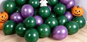 Glossy dark green and purple balloons clustered on a wooden floor beside Halloween pumpkins