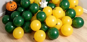 Green and yellow balloons arranged on a wood floor with a pumpkin, ghost and black spider accents