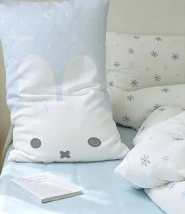 Pale blue and white bunny-shaped cushion on a bed with matching snowflake-print bedding