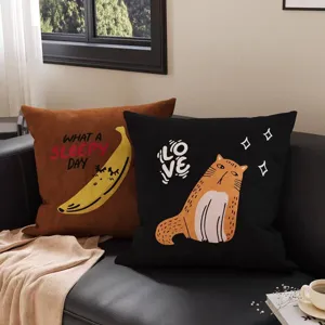 Zwei Samtkissen auf dunklem Sofa, mit Bananenmotiv und orangefarbener Katze samt LOVE-Aufdruck