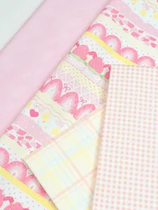 Overhead view of layered pink fabric with strawberry cake prints, solid pink and checked patterns