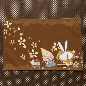 Flat view of a brown placemat with floral lace motifs and a playful cartoon pig and rabbit