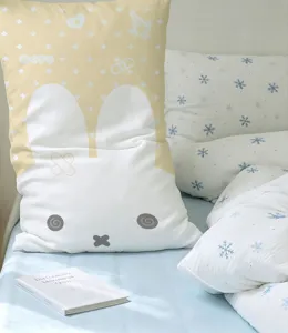 Yellow and white rabbit-print cushion cover displayed on a bed beside blue snowflake bedding