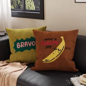 Zwei bedruckte Plüschkissen auf einem Sofa mit grünem BRAVO-Motiv und schläfriger Banane