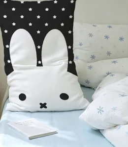 Rabbit-shaped cushion with a white face and black star-patterned ears, placed on a snowy-print bed