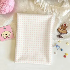 Flat lay of white fabric with pale pink checks, styled with yarn, lace and cute craft accents