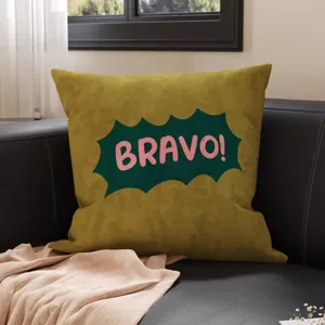Samtiges olivgrünes Kissen mit pinkem „BRAVO!“-Aufdruck, auf einem dunklen Ledersofa arrangiert