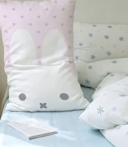 Layered bedding with a white rabbit-face cushion, pink stars, and blue snowflake-print pillows.