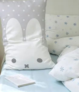Close-up of a white bunny cushion with gray star print beside blue snowflake bedding
