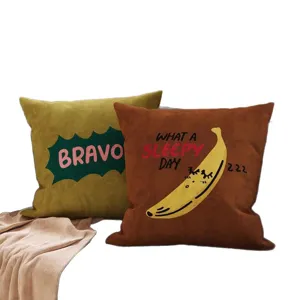 Zwei dekorative Plüschkissen: olivgrün mit BRAVO-Schriftzug und rostbraun mit Bananenmotiv