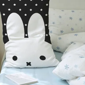 Long bunny-face cushion with a black star-print top, displayed on a softly styled bed