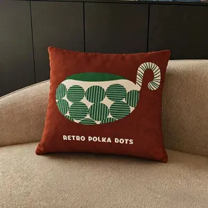 Coussin carré brun rouille, à pois rayés verts et inscription rétro, posé sur un canapé beige
