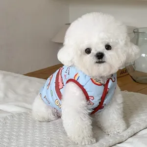 Petit chien blanc portant un gilet bleu à motif cartoon et bordure rouge sur une literie claire