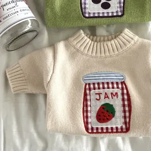 Detalle del tejido crema, cuello acanalado y parche de cuadros con un tarro de mermelada de fresa