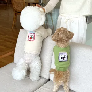 Dos perros sentados en sofá llevan jerséis de punto crema y verde con tarros de mermelada bordados.