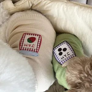 Detalle de jerséis de punto con parches de fresa y tarro de mermelada, en beige y verde